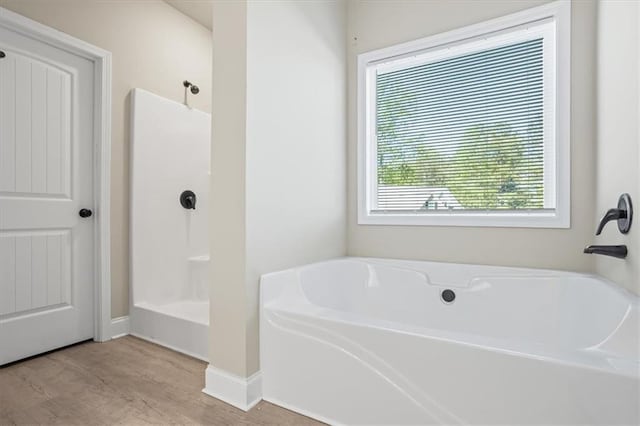 bathroom featuring a shower, wood finished floors, a tub to relax in, and baseboards