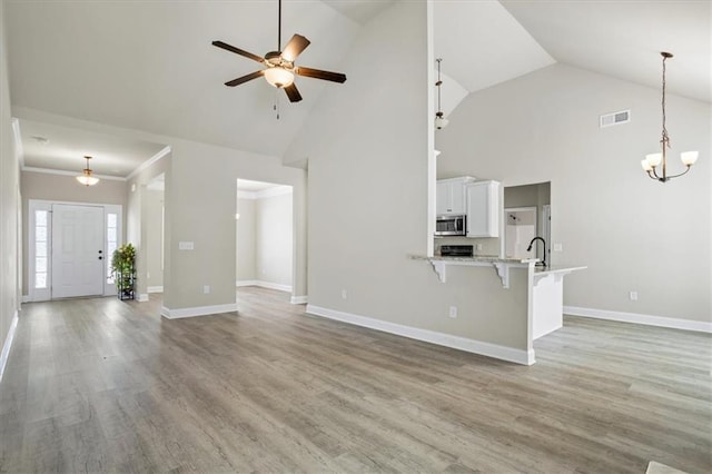 unfurnished living room featuring ceiling fan with notable chandelier, wood finished floors, baseboards, and visible vents