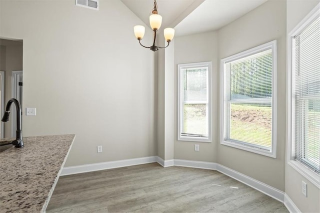 unfurnished dining area with a healthy amount of sunlight, wood finished floors, baseboards, and visible vents