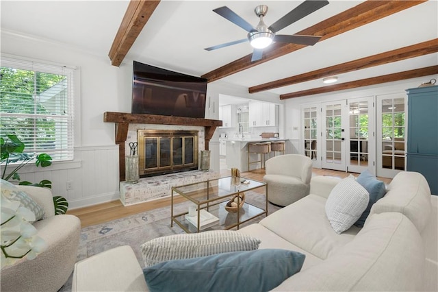 1104 Warrenhall Ln NE, Brookhaven, GA 30319 - living area featuring light wood-style floors, beamed ceiling, a ceiling fan, a wainscoted wall, and a glass covered fireplace