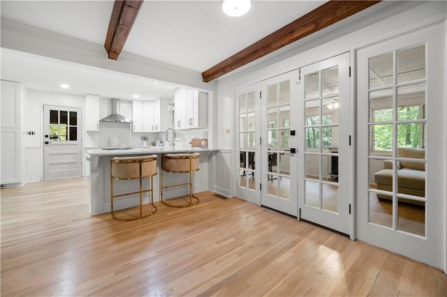 1104 Warrenhall Ln NE, Brookhaven, GA 30319 - kitchen with wall chimney range hood, beam ceiling, plenty of natural light, white cabinetry, and light wood-type flooring