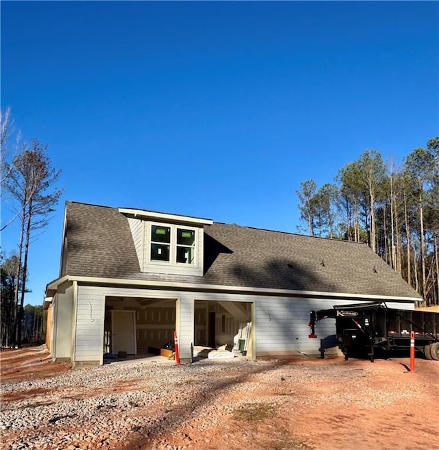 rear view of property with a garage, driveway, and roof with shingles