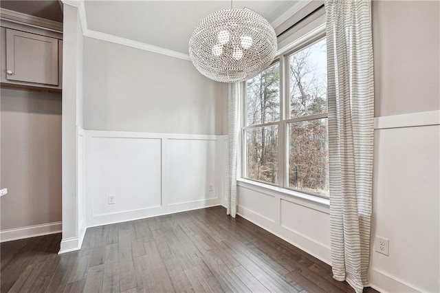 unfurnished dining area with a decorative wall, ornamental molding, dark wood-style flooring, and a notable chandelier