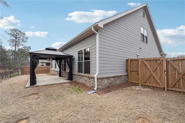 view of property exterior with brick siding, a gazebo, a gate, a patio area, and a fenced backyard