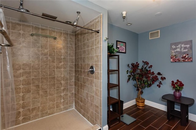 bathroom with baseboards, tiled shower, and wood finish floors