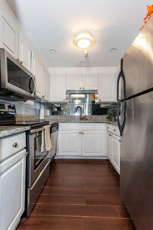 kitchen with stainless steel appliances, a sink, white cabinets, dark wood-type flooring, and stone counters
