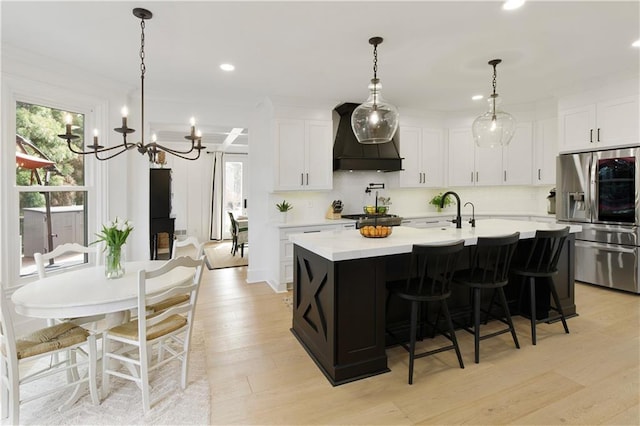 kitchen featuring premium range hood, light wood-style flooring, light countertops, stainless steel fridge, and tasteful backsplash