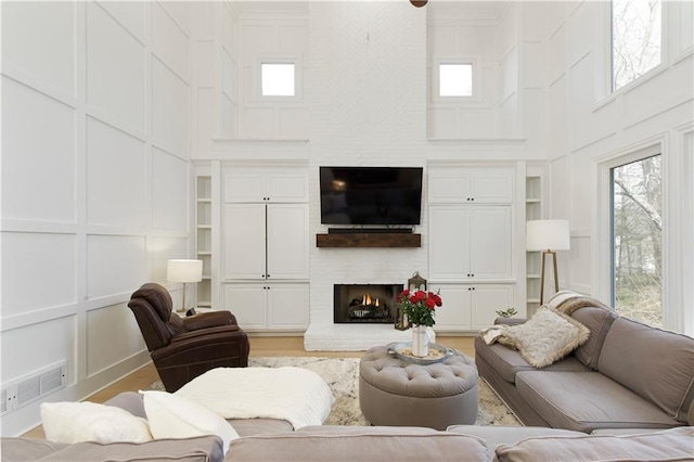 living room with built in shelves, a fireplace, visible vents, a decorative wall, and a towering ceiling