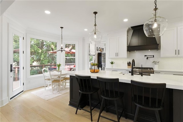 kitchen featuring white cabinets, light countertops, light wood-type flooring, premium range hood, and backsplash