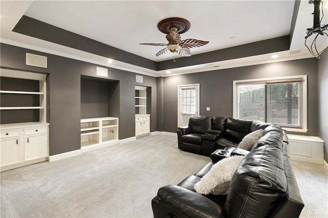 living room featuring built in features, a raised ceiling, light carpet, and baseboards