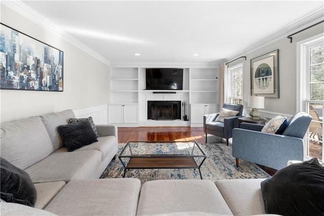 living area featuring a fireplace with raised hearth, recessed lighting, wood finished floors, built in features, and crown molding