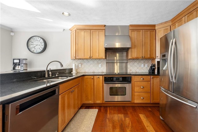 kitchen featuring dark countertops, dark wood-style floors, stainless steel appliances, wall chimney range hood, and a sink