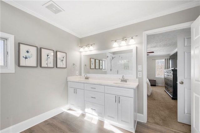 ensuite bathroom featuring visible vents, ornamental molding, a sink, tiled shower, and baseboards