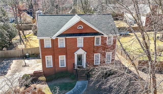 colonial house with a patio, brick siding, a shingled roof, and fence private yard