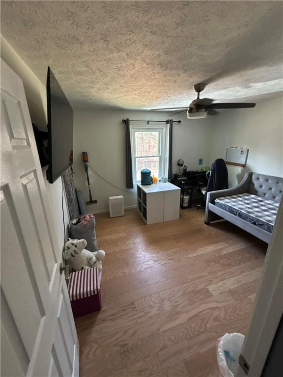 bedroom featuring light wood-style floors, a textured ceiling, baseboards, and ceiling fan