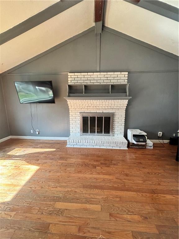 unfurnished living room featuring baseboards, vaulted ceiling with beams, wood finished floors, and a fireplace