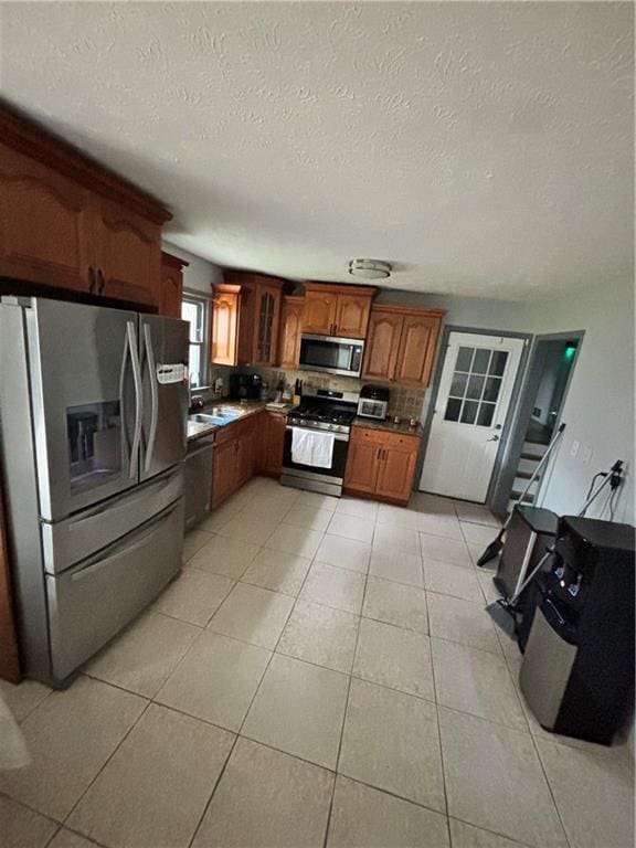 kitchen with light tile patterned floors, a textured ceiling, appliances with stainless steel finishes, and tasteful backsplash