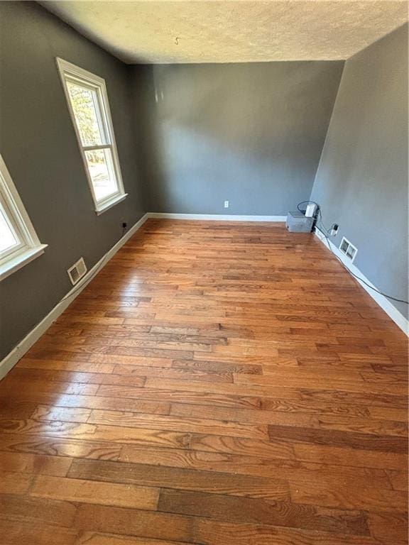 empty room featuring a textured ceiling, hardwood / wood-style floors, and visible vents