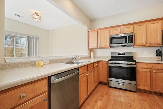 kitchen with appliances with stainless steel finishes, sink, and light wood-type flooring