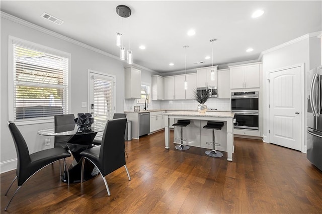 kitchen with stainless steel appliances, a sink, ornamental molding, tasteful backsplash, and a kitchen bar