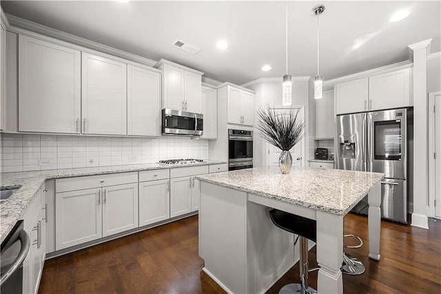 kitchen featuring appliances with stainless steel finishes, dark wood finished floors, a center island, backsplash, and ornamental molding