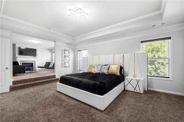carpeted bedroom featuring a tray ceiling, crown molding, a glass covered fireplace, and baseboards
