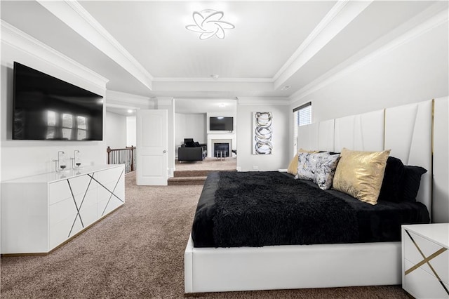 bedroom featuring carpet flooring, ornamental molding, a raised ceiling, and a glass covered fireplace