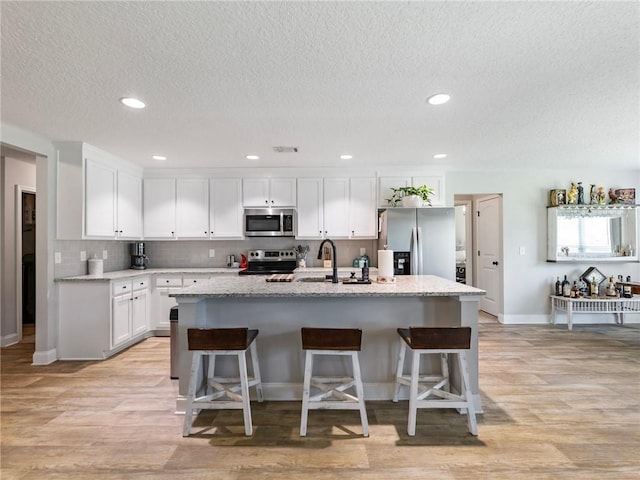 132 Mcmillian Ct, Winder, GA 30680 - kitchen featuring stainless steel appliances, a sink, white cabinetry, a center island with sink, and a breakfast bar