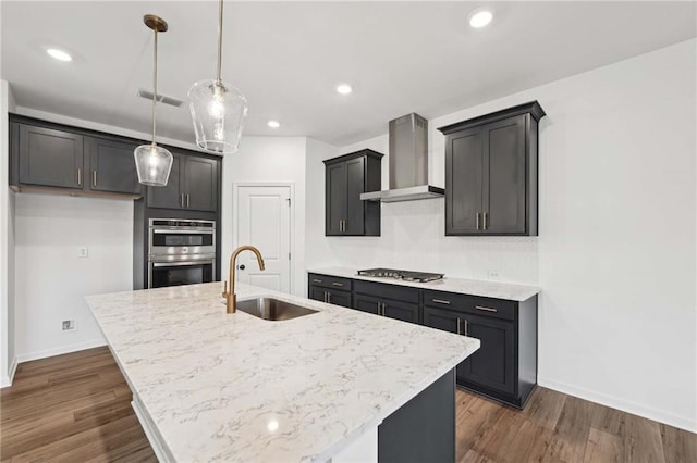 kitchen featuring sink, wall chimney range hood, hanging light fixtures, and a center island with sink