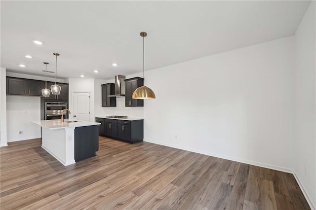 kitchen with sink, hanging light fixtures, hardwood / wood-style flooring, a center island with sink, and wall chimney exhaust hood