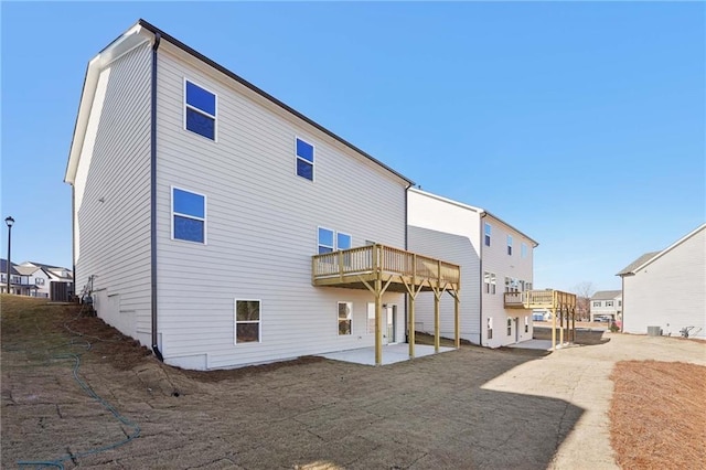 rear view of property with a wooden deck, central AC unit, and a patio area