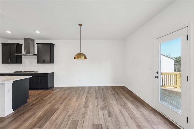 kitchen with wood-type flooring, decorative light fixtures, stainless steel gas cooktop, and wall chimney range hood