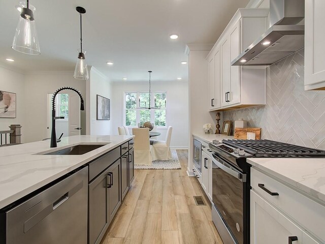 kitchen with appliances with stainless steel finishes, hanging light fixtures, sink, white cabinets, and a center island with sink