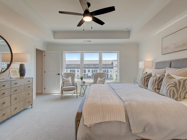 bedroom featuring ceiling fan, light colored carpet, and a tray ceiling