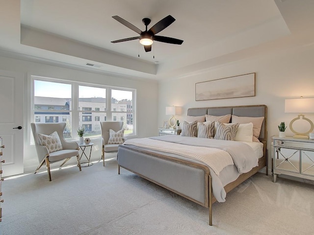 carpeted bedroom with ceiling fan and a tray ceiling