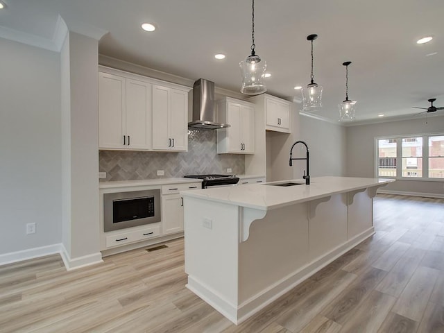 kitchen featuring sink, wall chimney range hood, a kitchen island with sink, and built in microwave