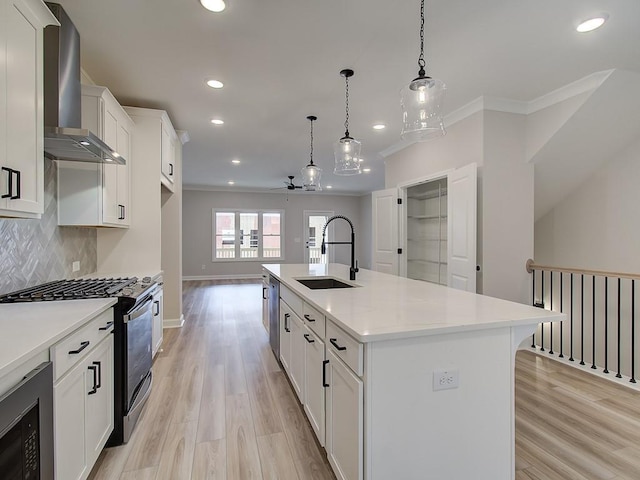 kitchen with pendant lighting, appliances with stainless steel finishes, sink, wall chimney range hood, and a center island with sink