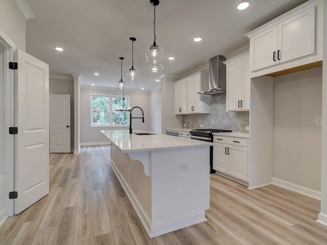 kitchen with white cabinets, decorative light fixtures, wall chimney range hood, sink, and a center island with sink