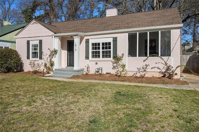 single story home featuring brick siding, a chimney, a front yard, and roof with shingles