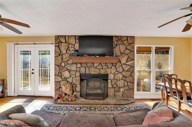 living room with wood-type flooring, ceiling fan, a fireplace, and french doors