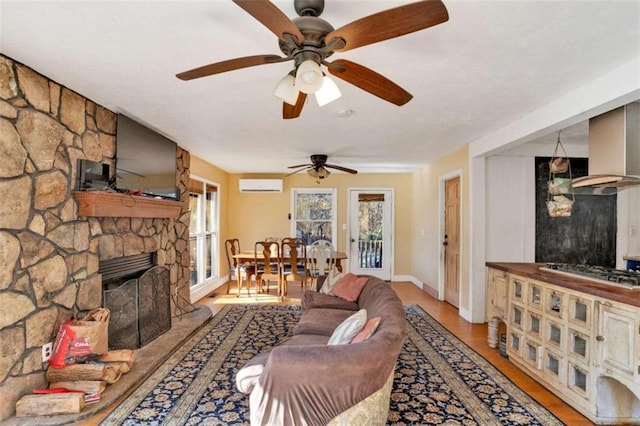 living room featuring a stone fireplace, a wall mounted air conditioner, and light hardwood / wood-style flooring