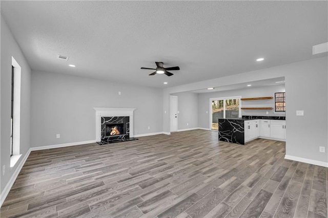 unfurnished living room featuring a textured ceiling, light hardwood / wood-style floors, ceiling fan, and a premium fireplace