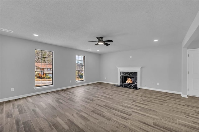 unfurnished living room with a high end fireplace, light hardwood / wood-style floors, and a textured ceiling