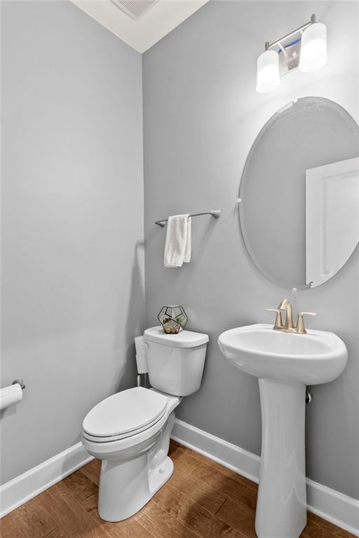 half bath featuring baseboards, wood finished floors, and toilet