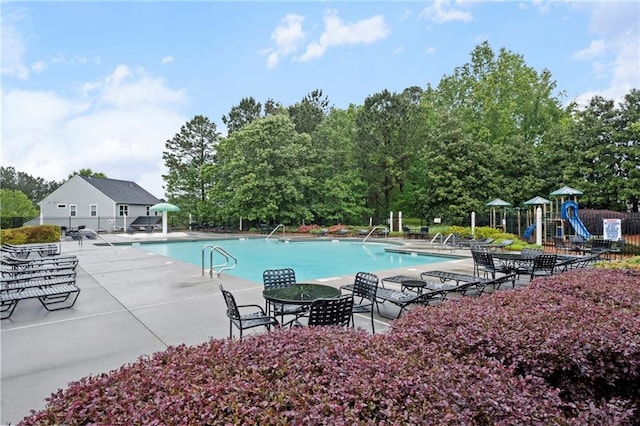 community pool with fence, a patio, and view of wooded area