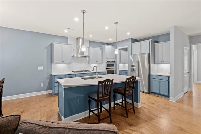 kitchen featuring stainless steel appliances, wall chimney exhaust hood, a sink, backsplash, and light countertops