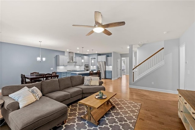 living area featuring stairway, ceiling fan, light wood-style floors, baseboards, and a chandelier