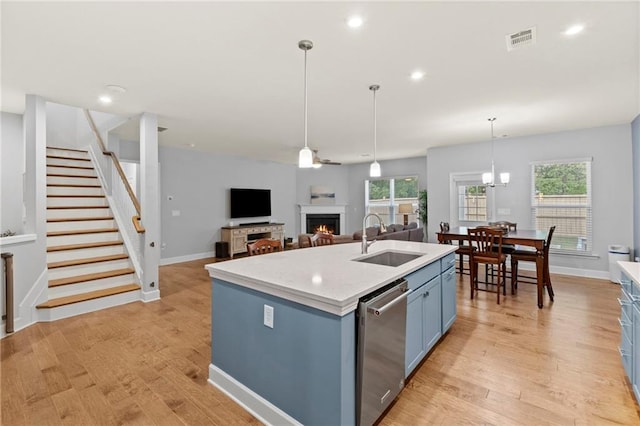 kitchen featuring a sink, stainless steel dishwasher, blue cabinetry, a lit fireplace, and light countertops