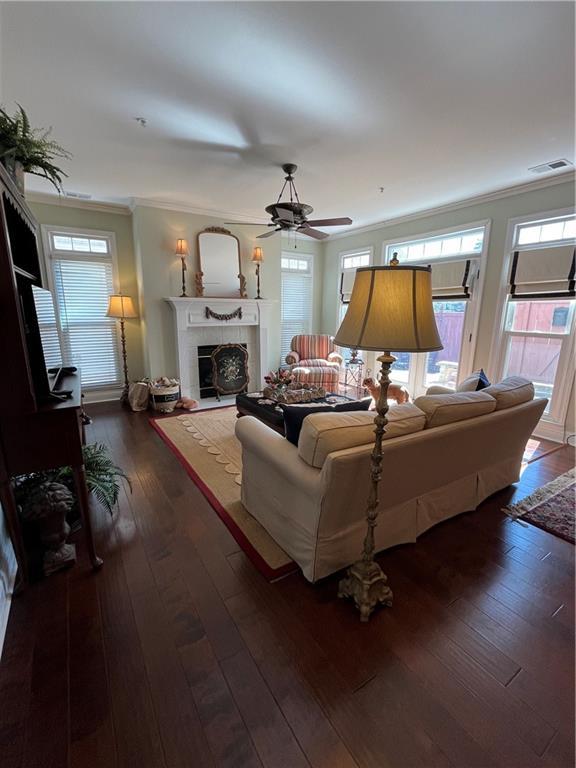 living area featuring visible vents, crown molding, a tiled fireplace, hardwood / wood-style floors, and a wealth of natural light