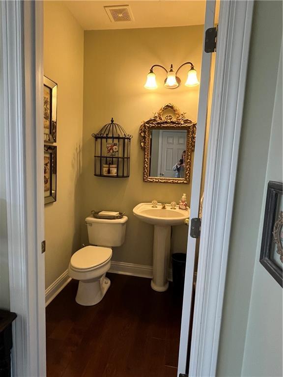 half bathroom with toilet, wood finished floors, visible vents, and baseboards